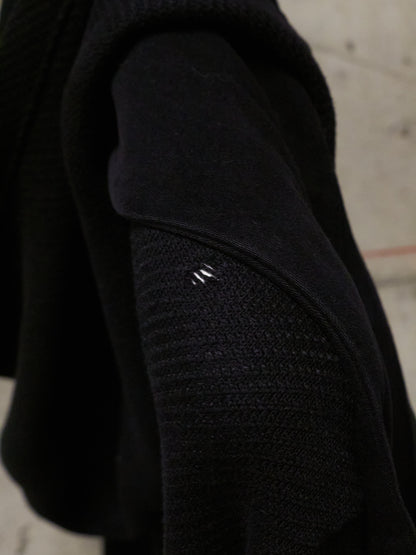 Close-up of a black textured sleeve with a brand logo on a concrete surface.
