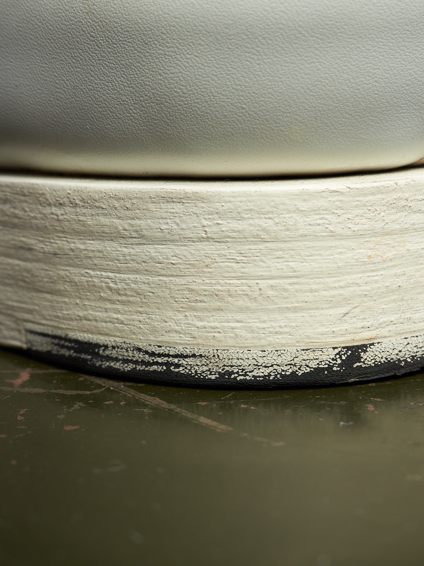Close-up of a ceramic vessel showing a thick, textured off-white painted rim with a black unglazed edge, resting on a dark olive-green surface.