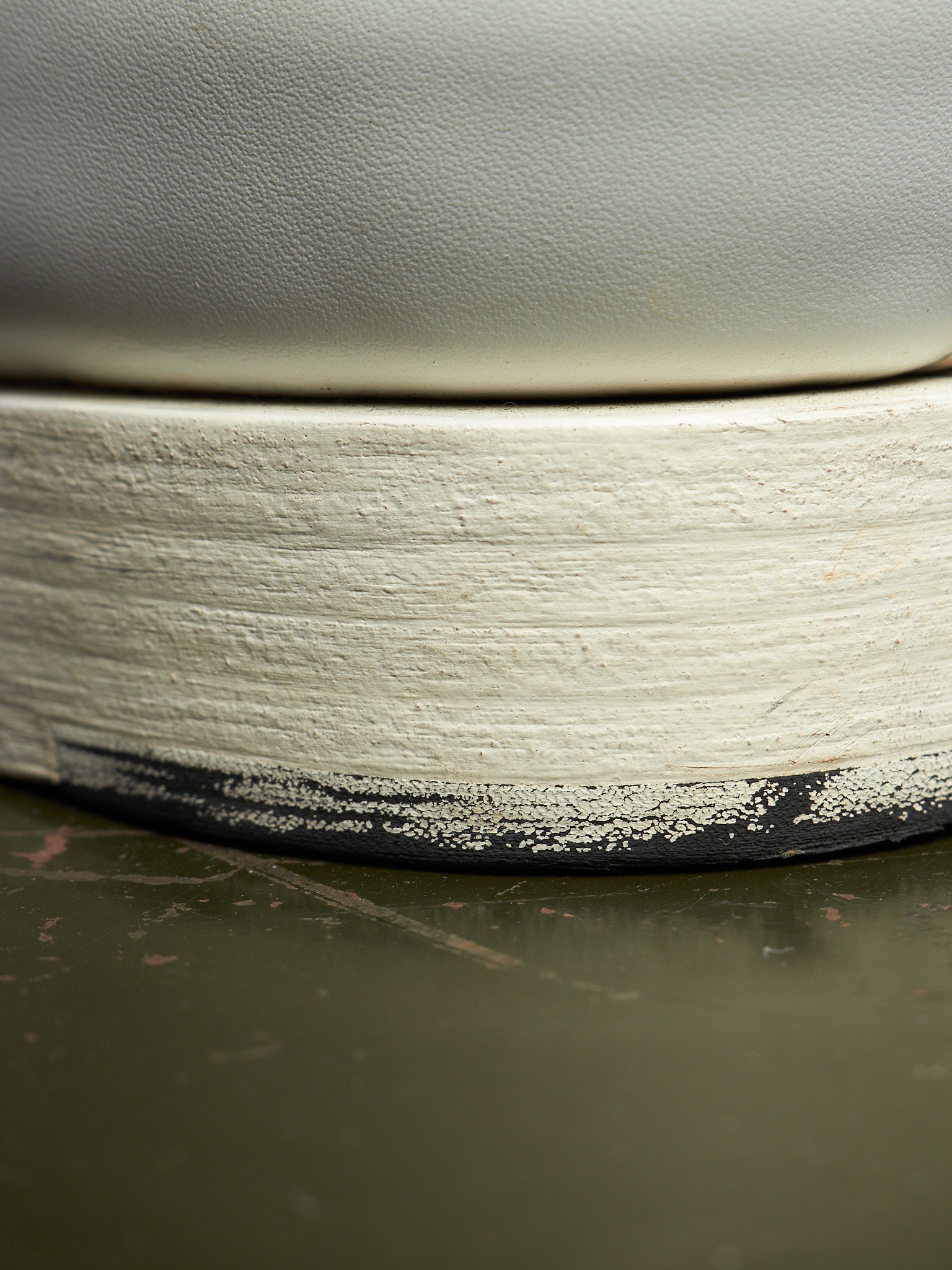 Close-up of a ceramic vessel showing a thick, textured off-white painted rim with a black unglazed edge, resting on a dark olive-green surface.