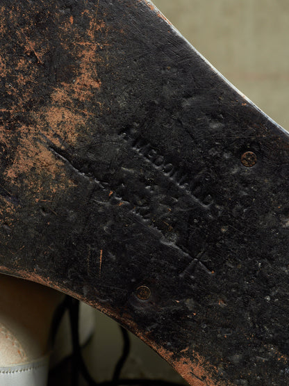 Close-up of the underside of a dark wooden axe or hatchet blade, showing weathered wood grain, rust-like discoloration, and stamped markings.