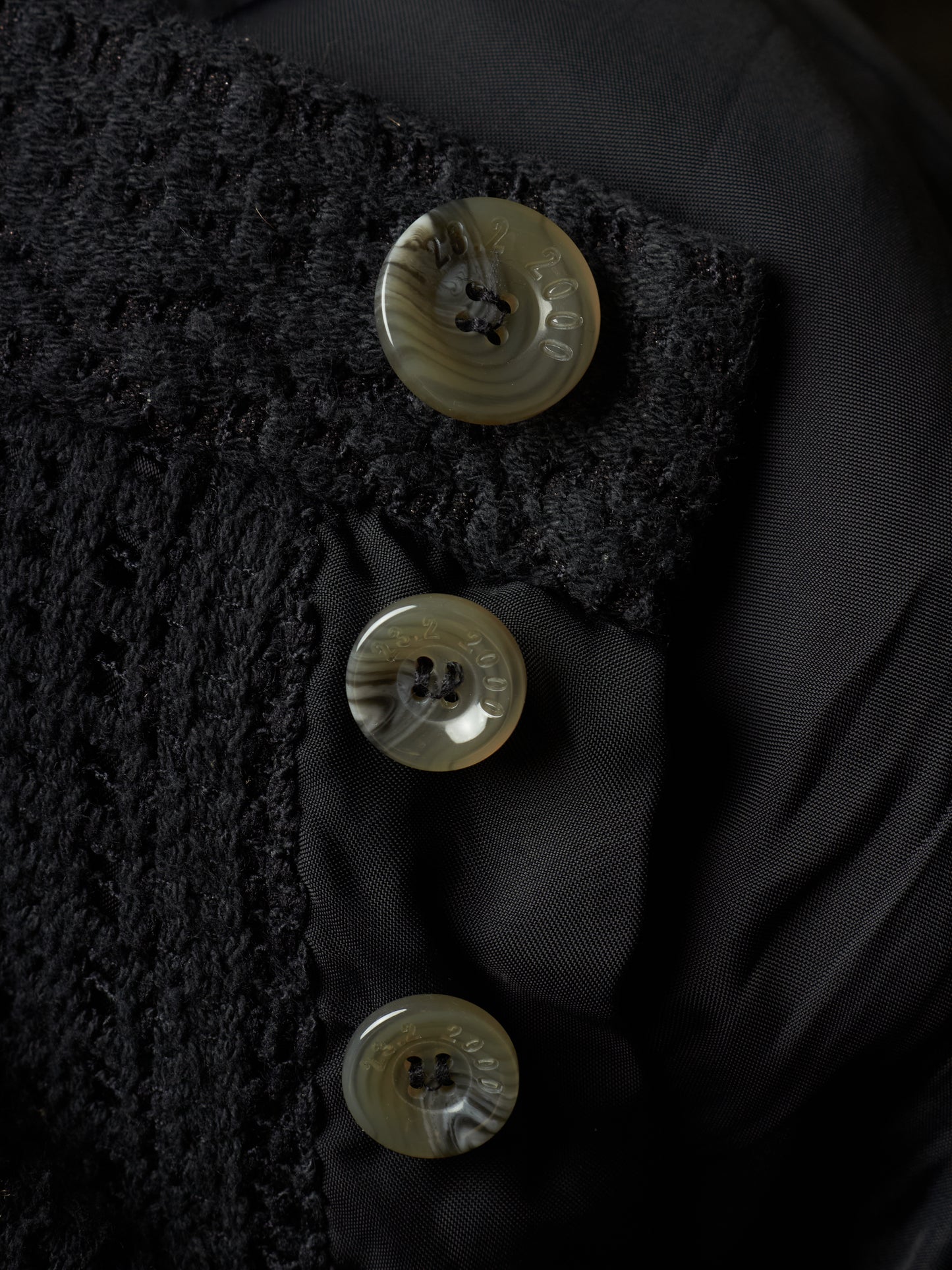 Close-up of a black textured jacket with three round shell buttons on a black satin lining.