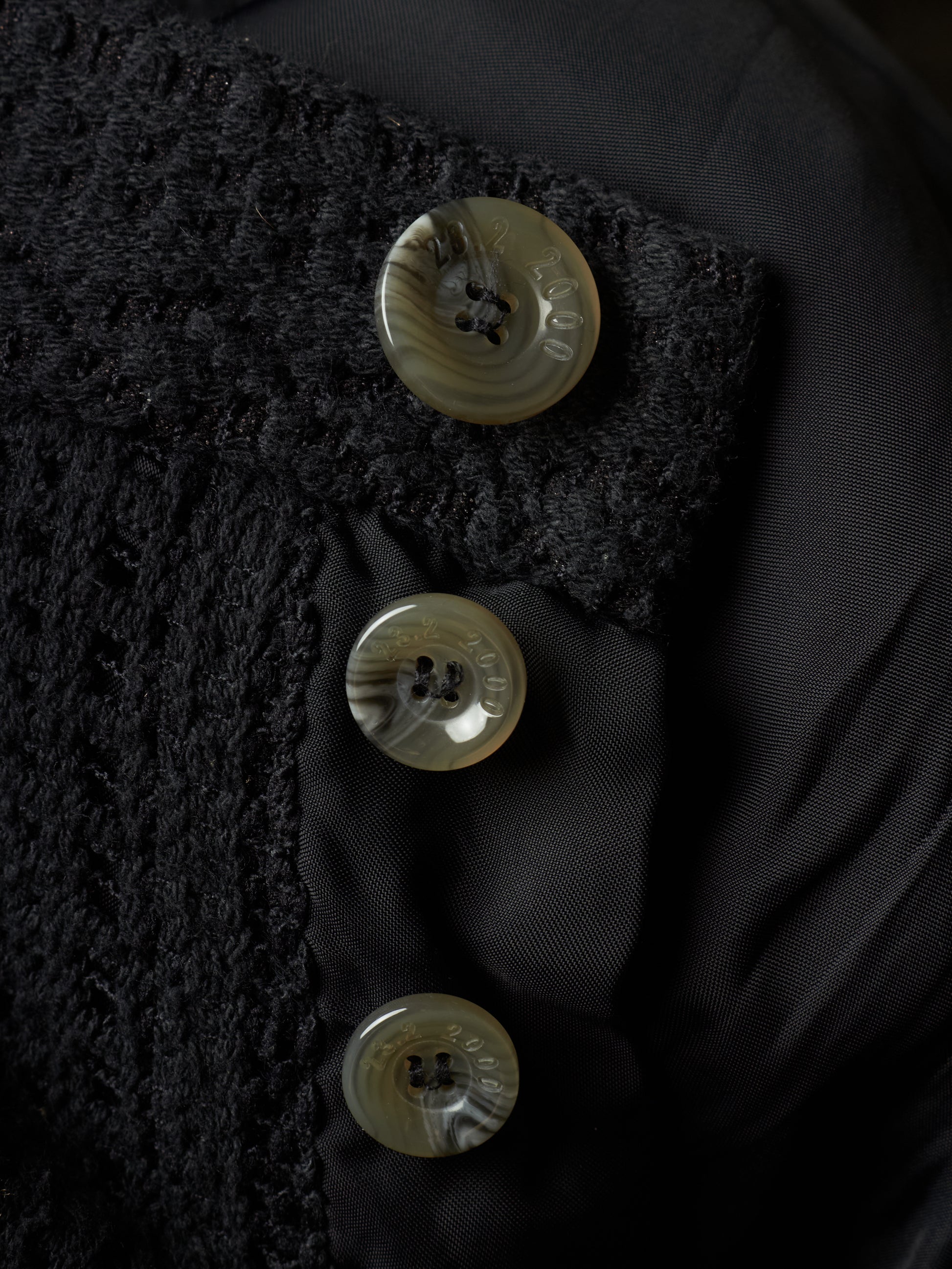 Close-up of a black textured jacket with three round shell buttons on a black satin lining.