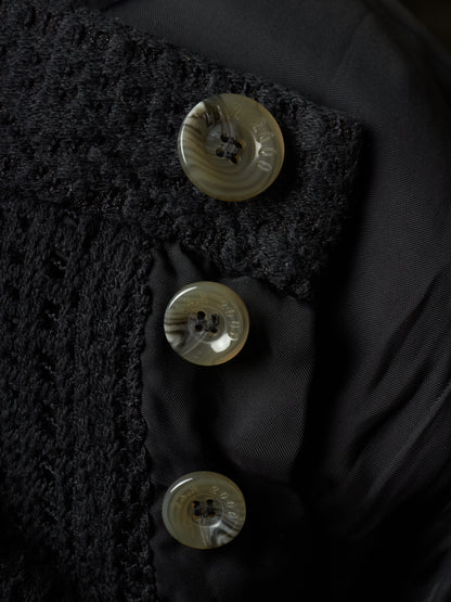 Close-up of a black textured jacket with three round shell buttons on a black satin lining.