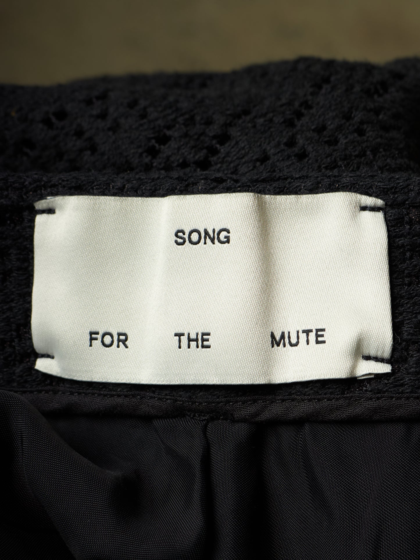 Close-up of a black knit garment with a white fabric label reading 'SONG FOR THE MUTE'.
