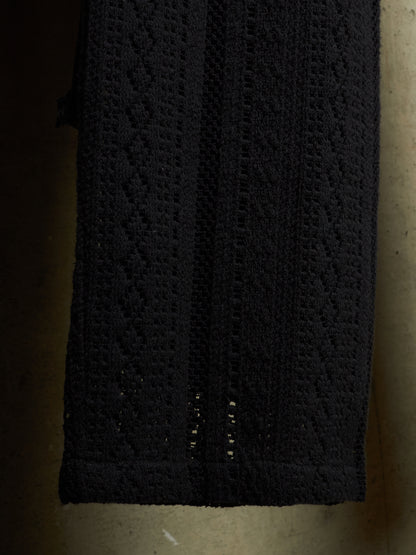 A close-up of a black textured knit fabric, showing a diamond-patterned crochet or lace design with openwork details near the bottom edge.
