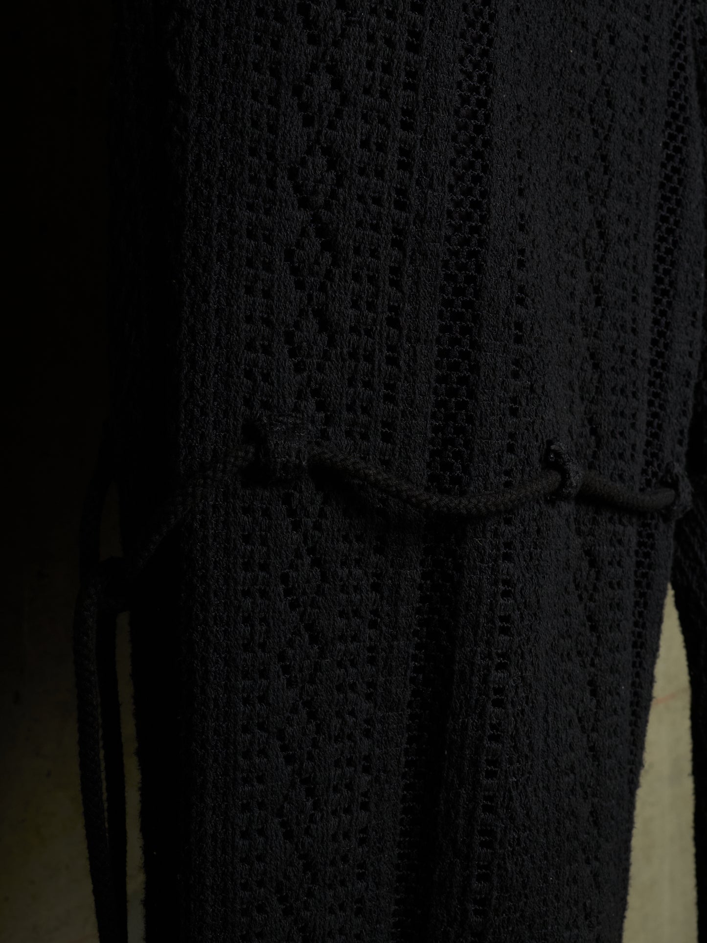 Close-up of a black textured knit garment with a diamond cable pattern and a drawstring tie at the waist.