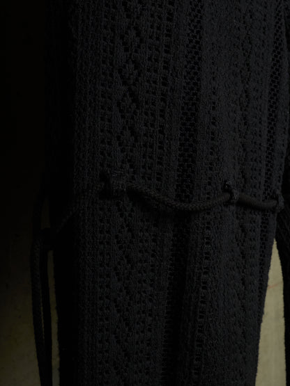 Close-up of a black textured knit garment with a diamond cable pattern and a drawstring tie at the waist.