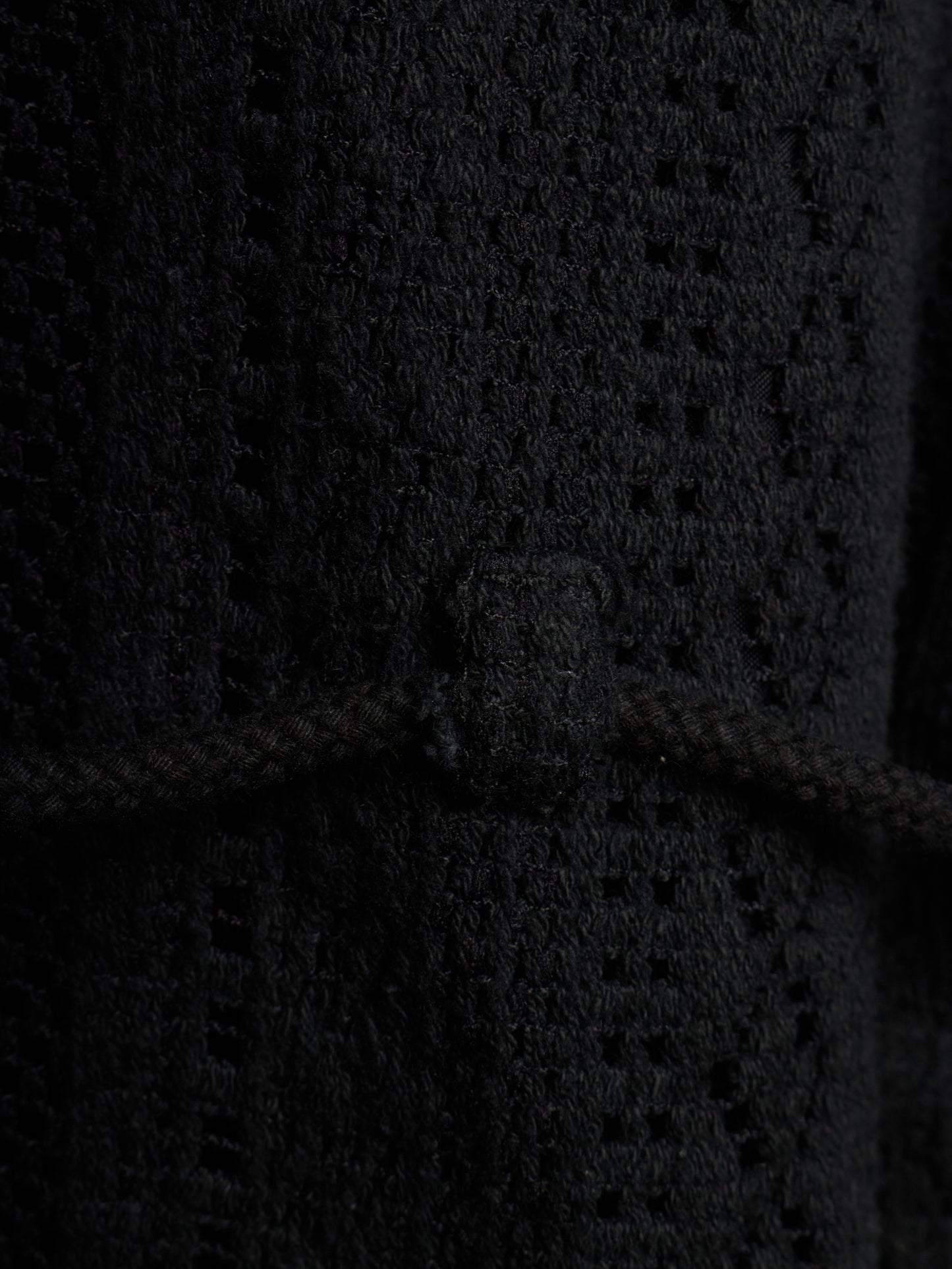 Close-up of a black textured knit garment with a braided cord detail and a small rectangular tab at the center.