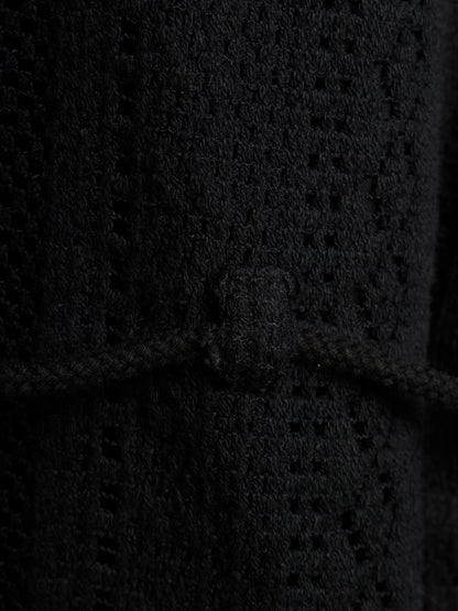 Close-up of a black textured knit garment with a braided cord detail and a small rectangular tab at the center.