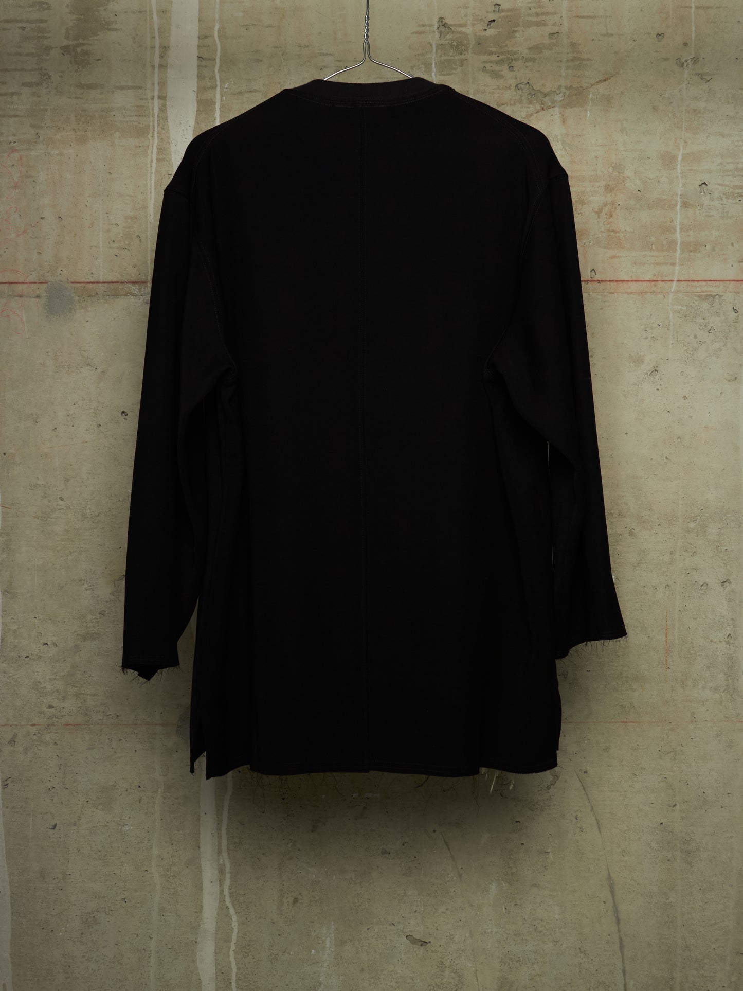 A black long-sleeve top hanging on a wire hanger against a textured concrete wall.