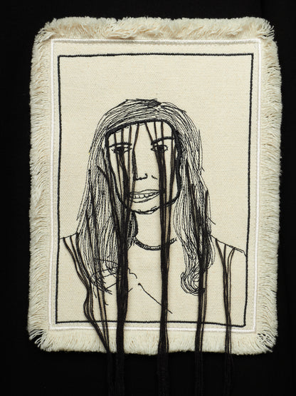 A square textile artwork or pillow cover with a cream woven background, black stitched portrait lines, and long black hanging threads in front, shown against a black background.