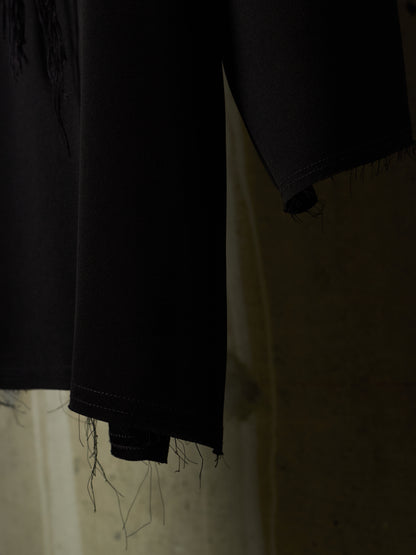 Close-up of a black garment with frayed, unfinished hems hanging against a dimly lit beige background.