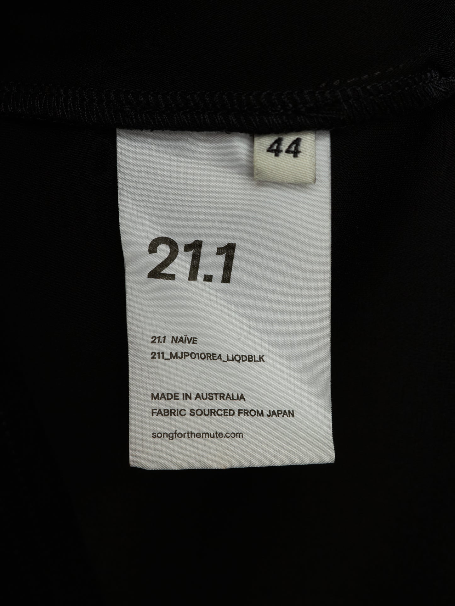 A close-up of a white garment size and color label sewn onto a black garment. The label reads 21.