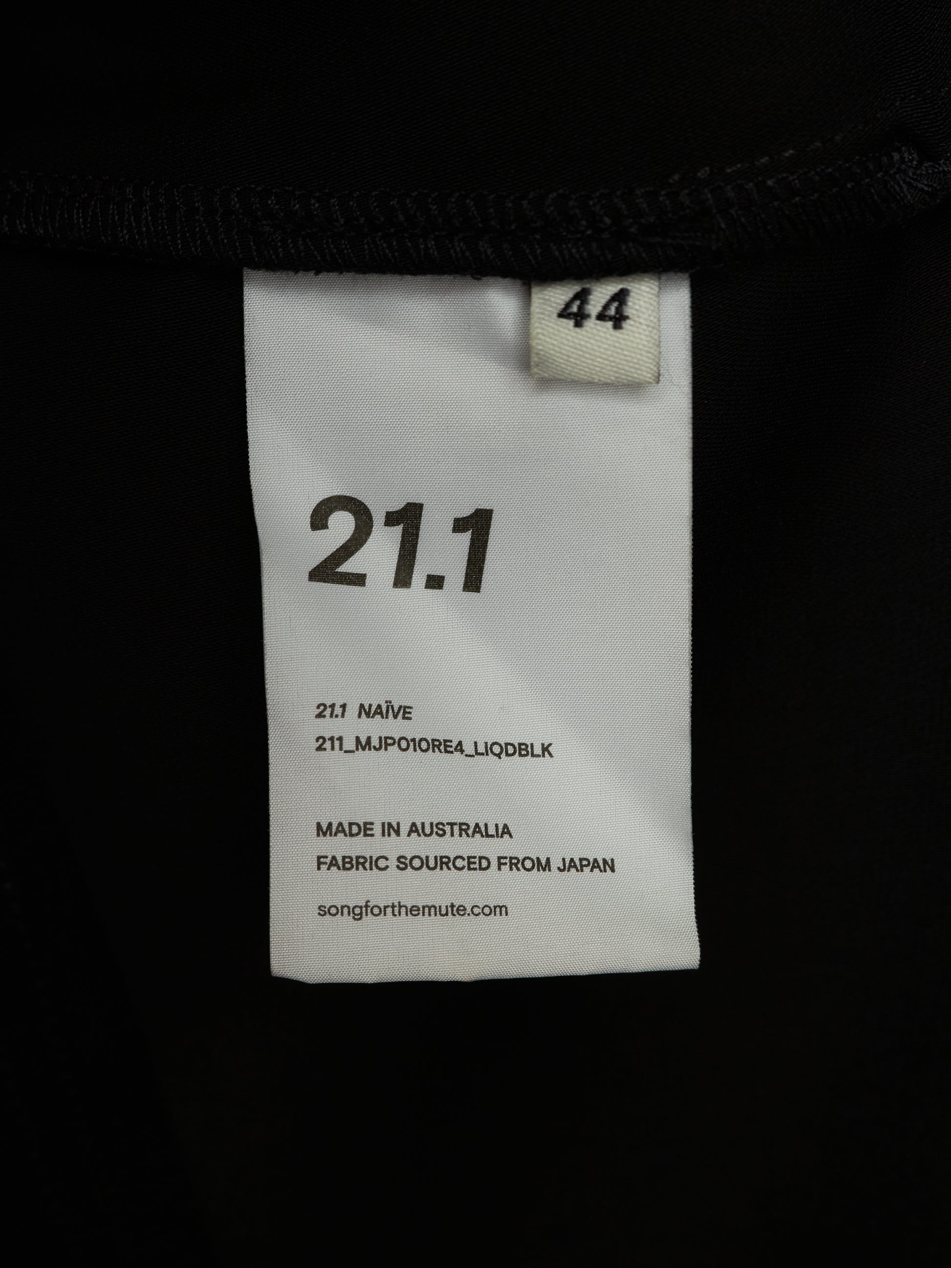A close-up of a white garment size and color label sewn onto a black garment. The label reads 21.