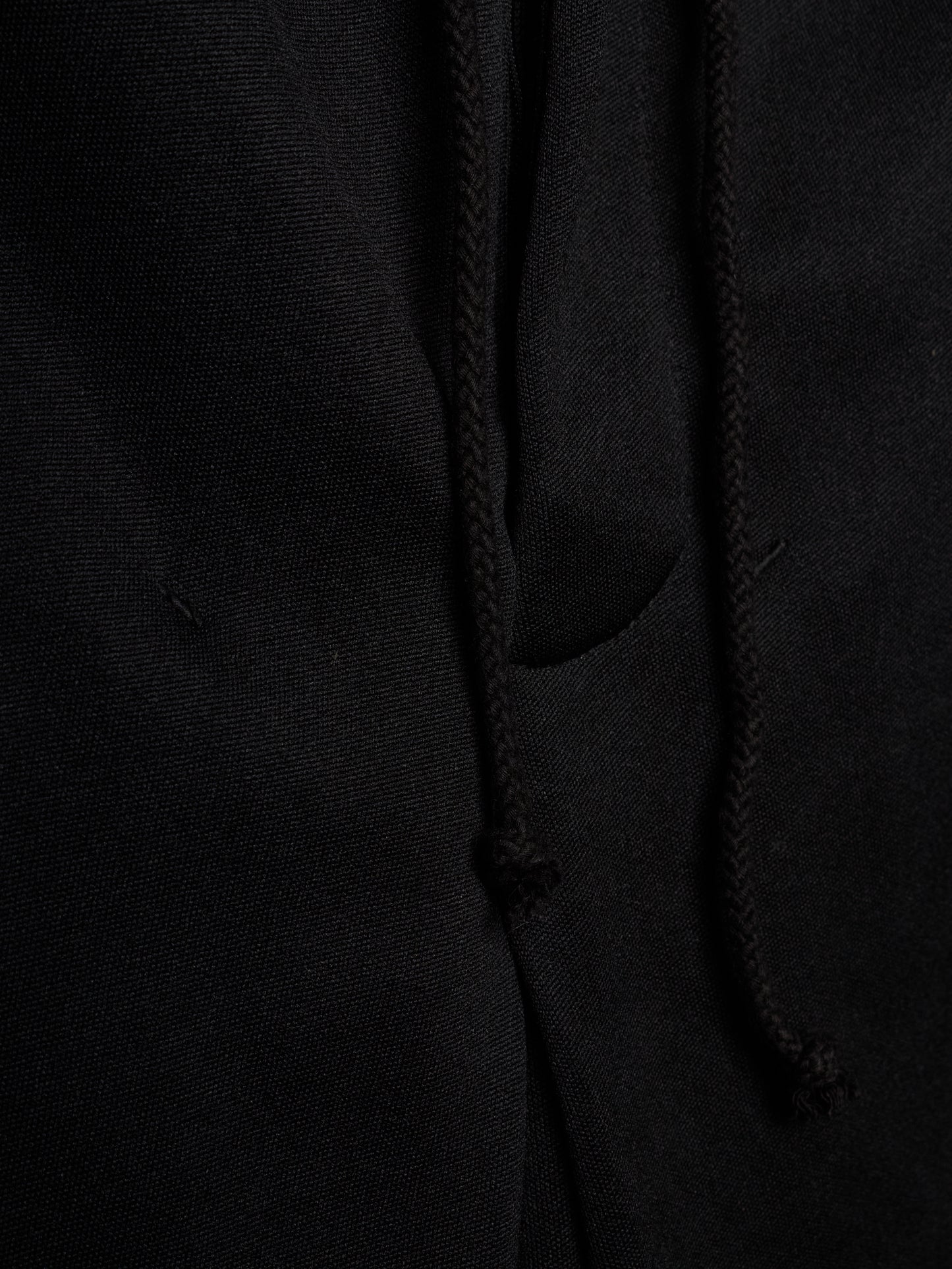 Close-up of a black fabric garment showing a drawstring and a side pocket, with the texture of the material clearly visible.