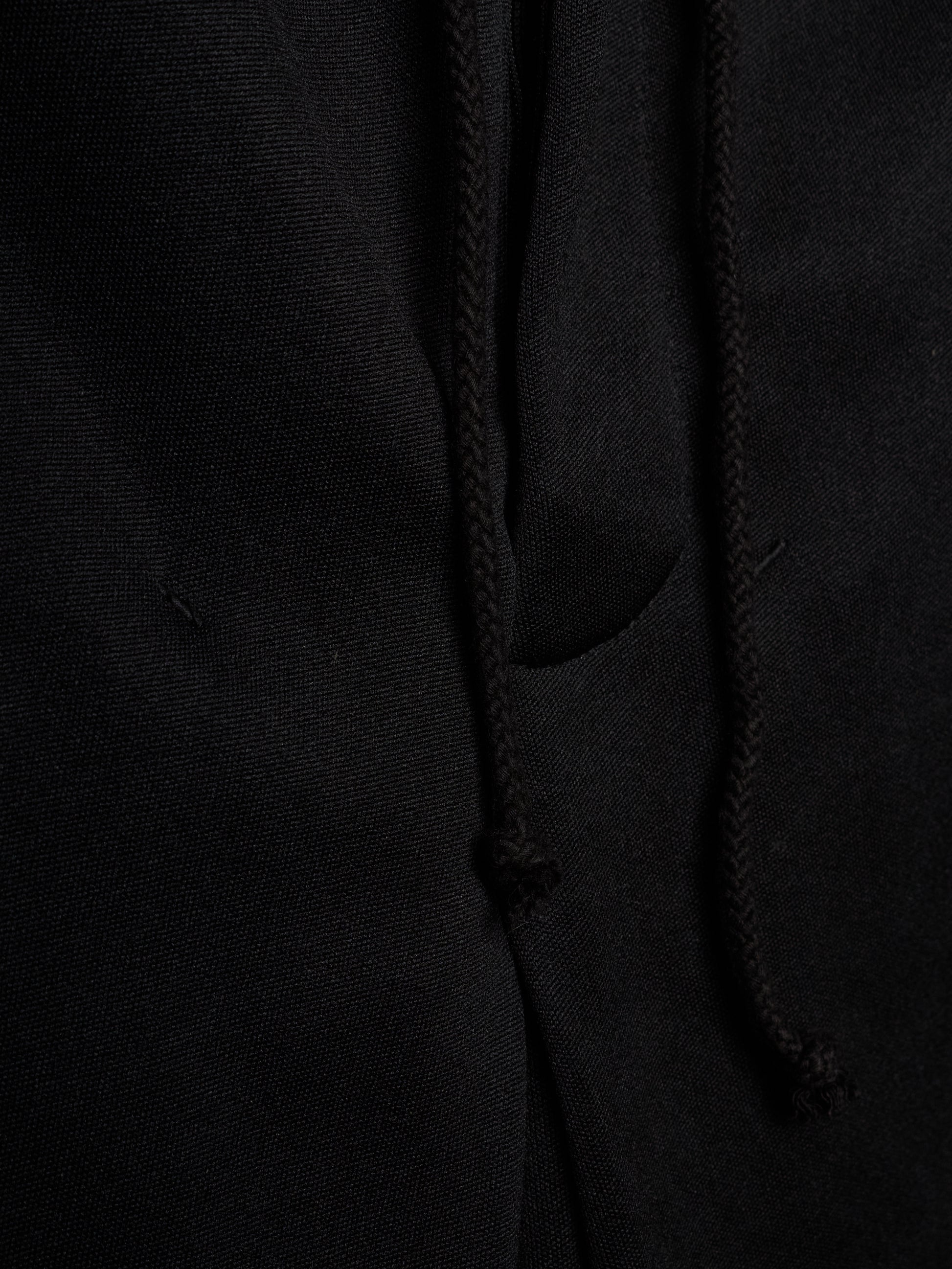 Close-up of a black fabric garment showing a drawstring and a side pocket, with the texture of the material clearly visible.