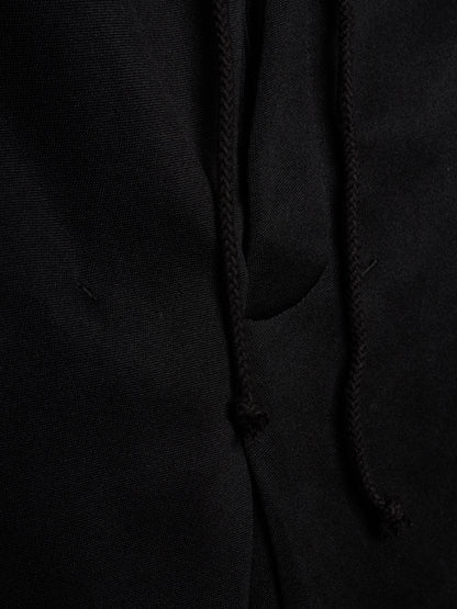 Close-up of a black fabric garment showing a drawstring and a side pocket, with the texture of the material clearly visible.