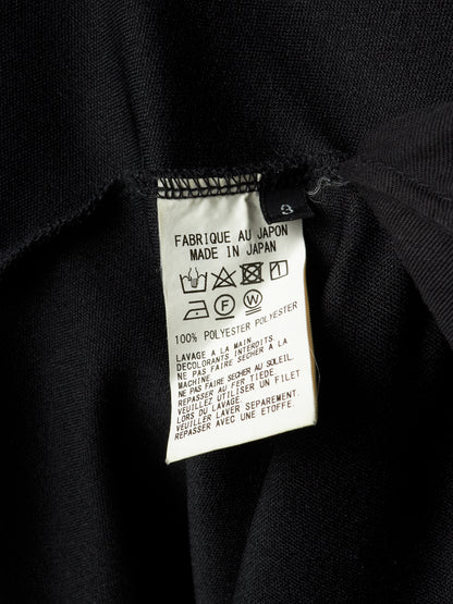 Close-up of a black garment's interior label showing 'FABRIQUE AU JAPON MADE IN JAPAN', '100% POLYESTER', and care symbols on a white paper tag.