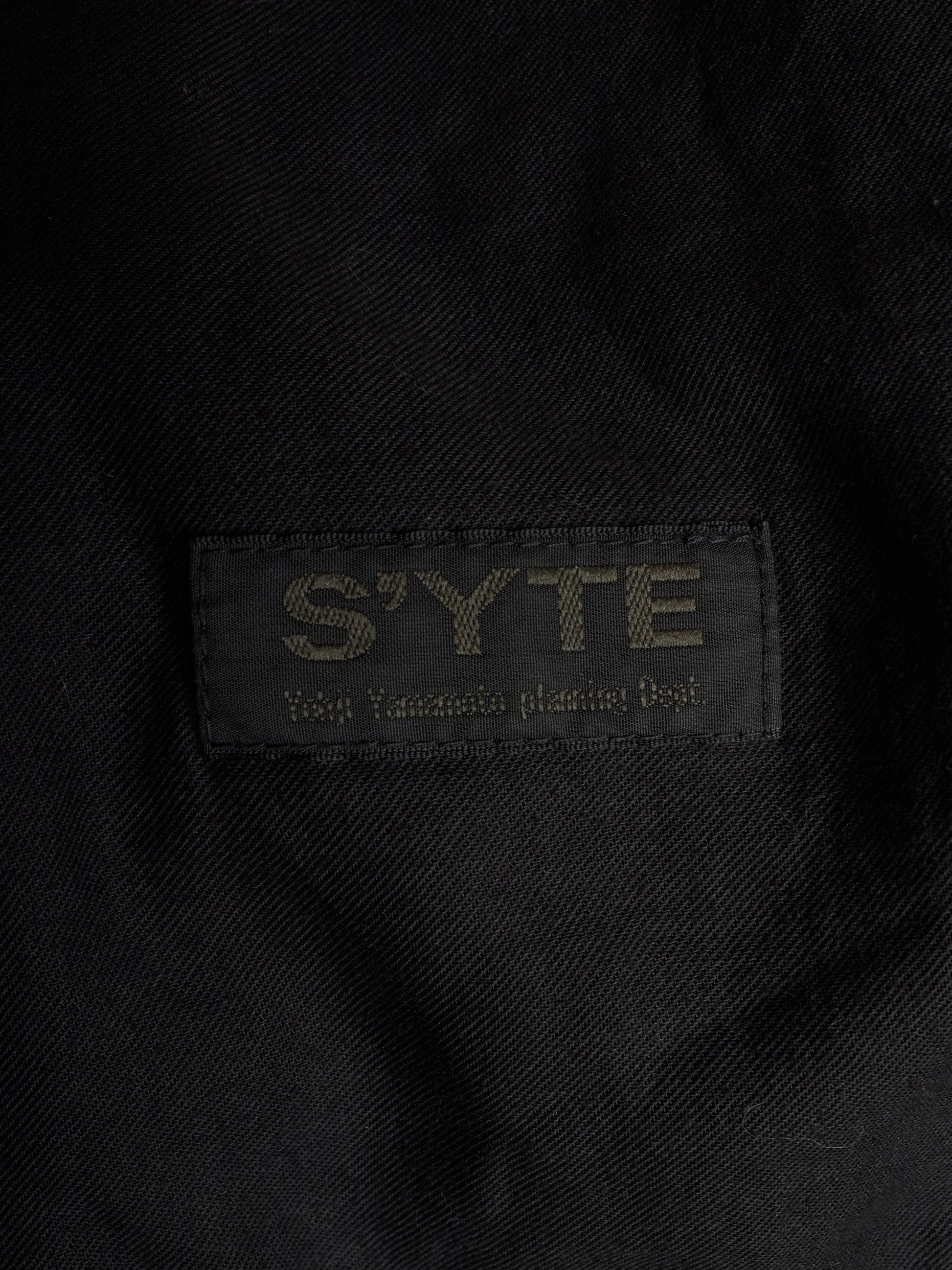 Close-up of a black woven fabric label with the brand name 'S'YTE' and the text 'Yokohama plastic bag' stitched in a contrasting light tone.