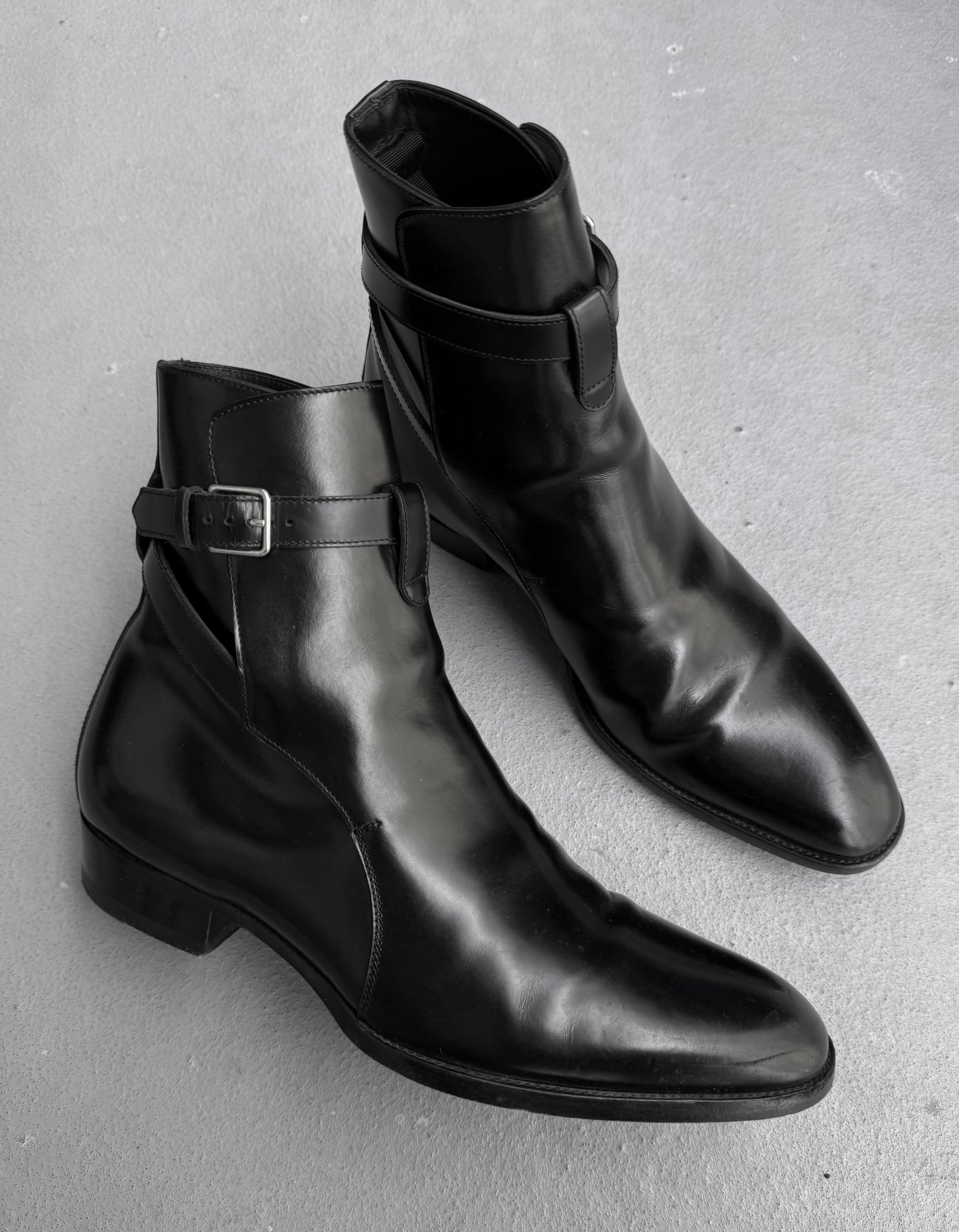 Pair of black leather boots with buckle details on a gray background