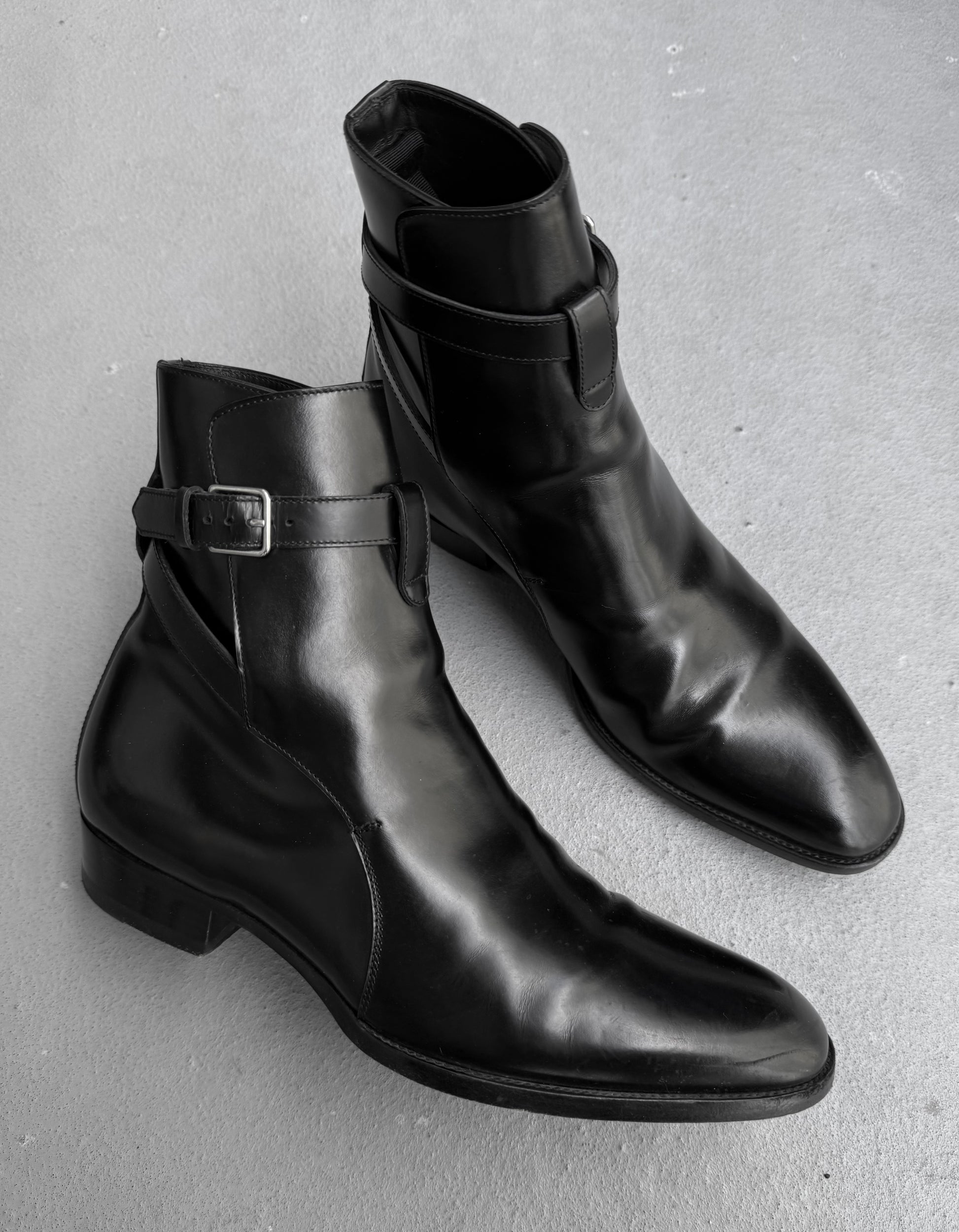 Pair of black leather boots with buckle details on a gray background
