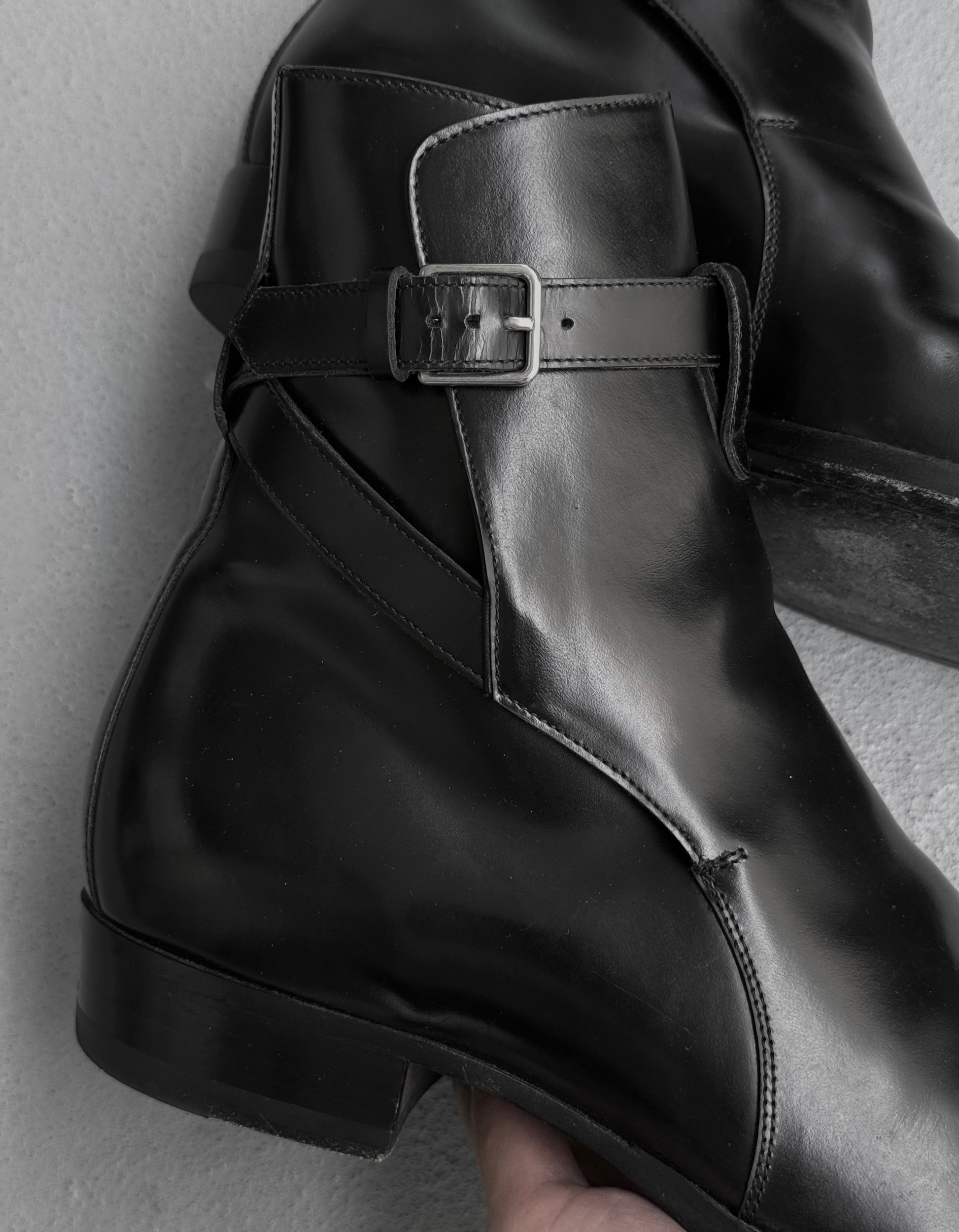 Black leather boot with a buckle on a neutral background