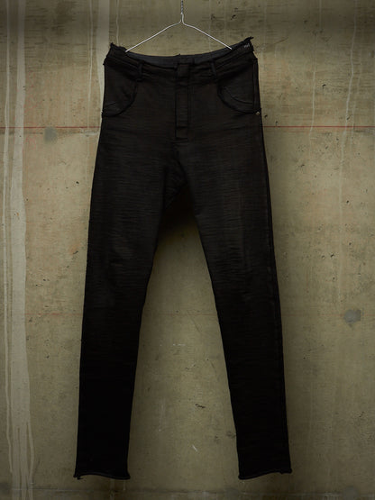 Black slim-fit jeans hanging on a metal hanger against a textured concrete wall.