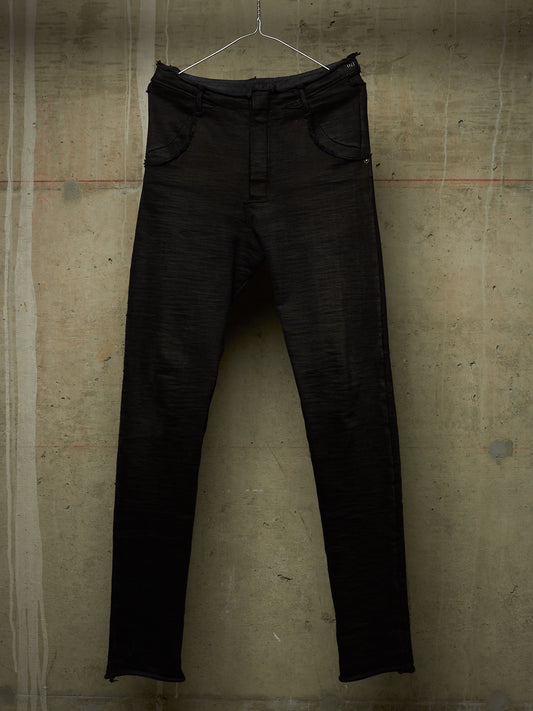 Black slim-fit jeans hanging on a metal hanger against a textured concrete wall.