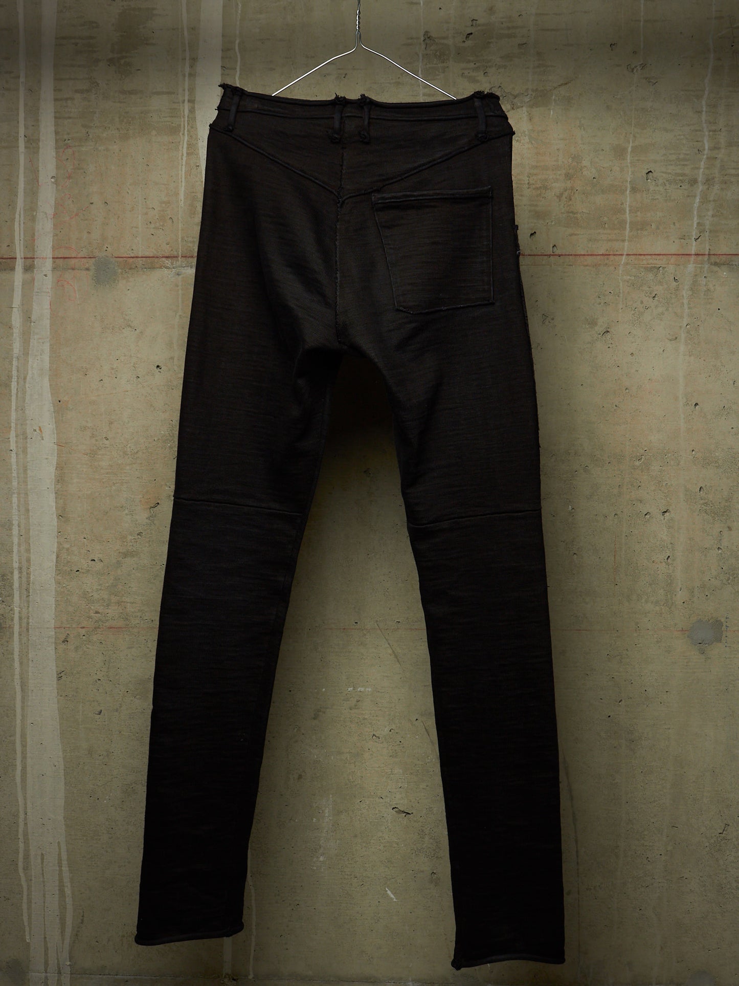Black slim-fit jeans hanging on a wire hanger against a textured concrete wall.