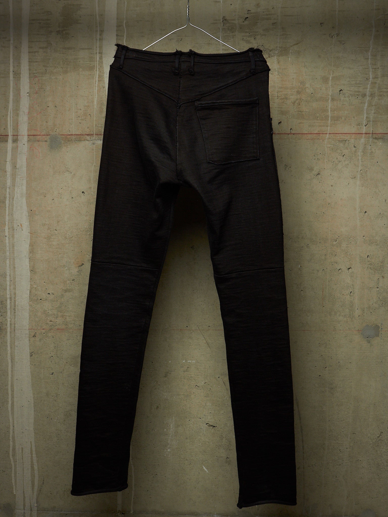 Black slim-fit jeans hanging on a wire hanger against a textured concrete wall.