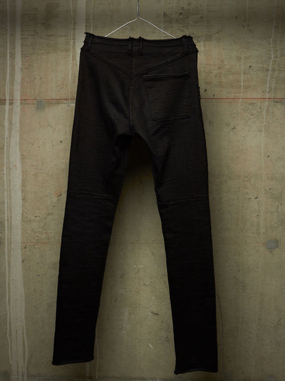 Black slim-fit jeans hanging on a wire hanger against a textured concrete wall.
