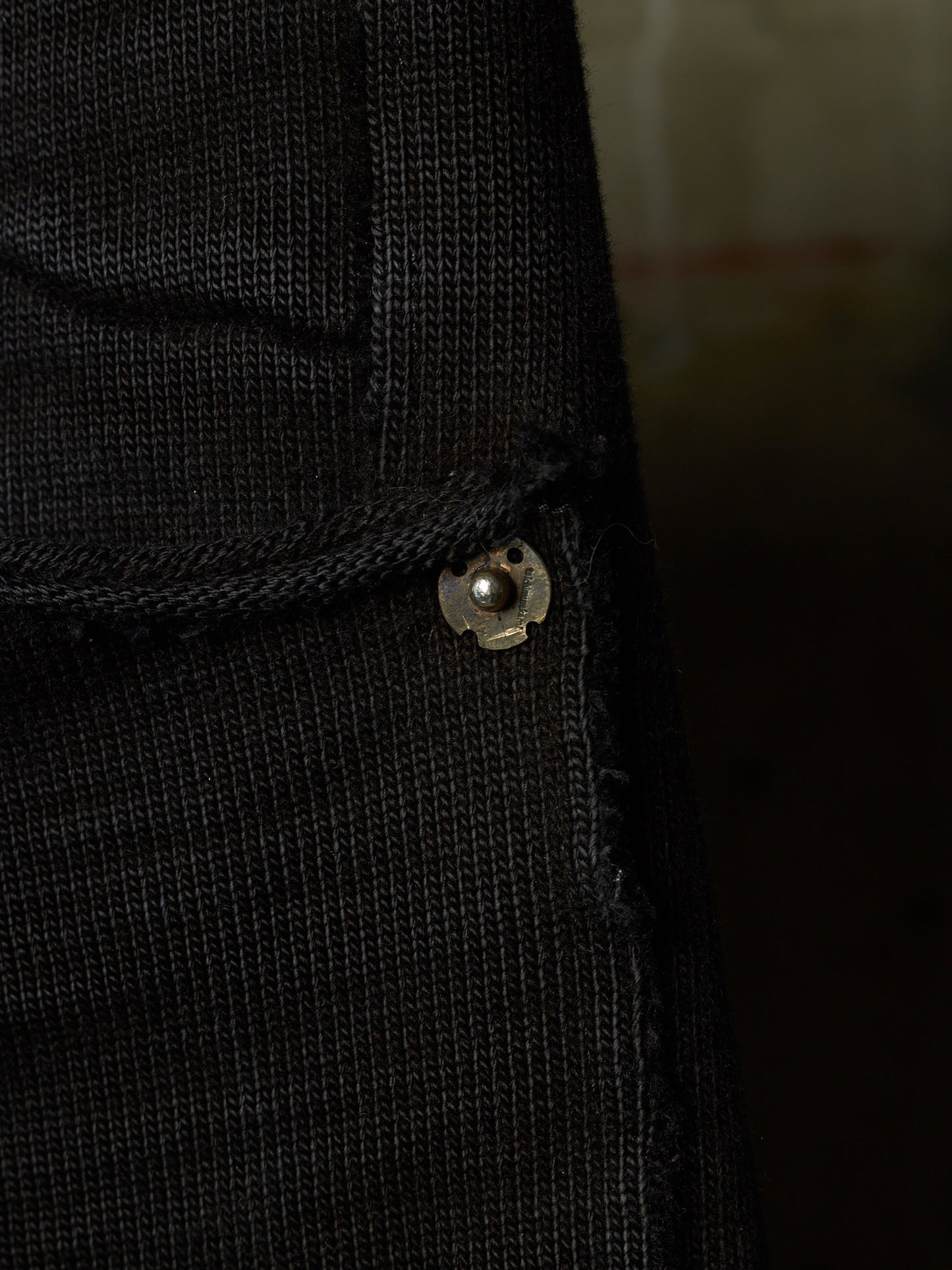Close-up of a black ribbed knit garment, likely a sweater or jacket, showing a small metallic snap button detail.