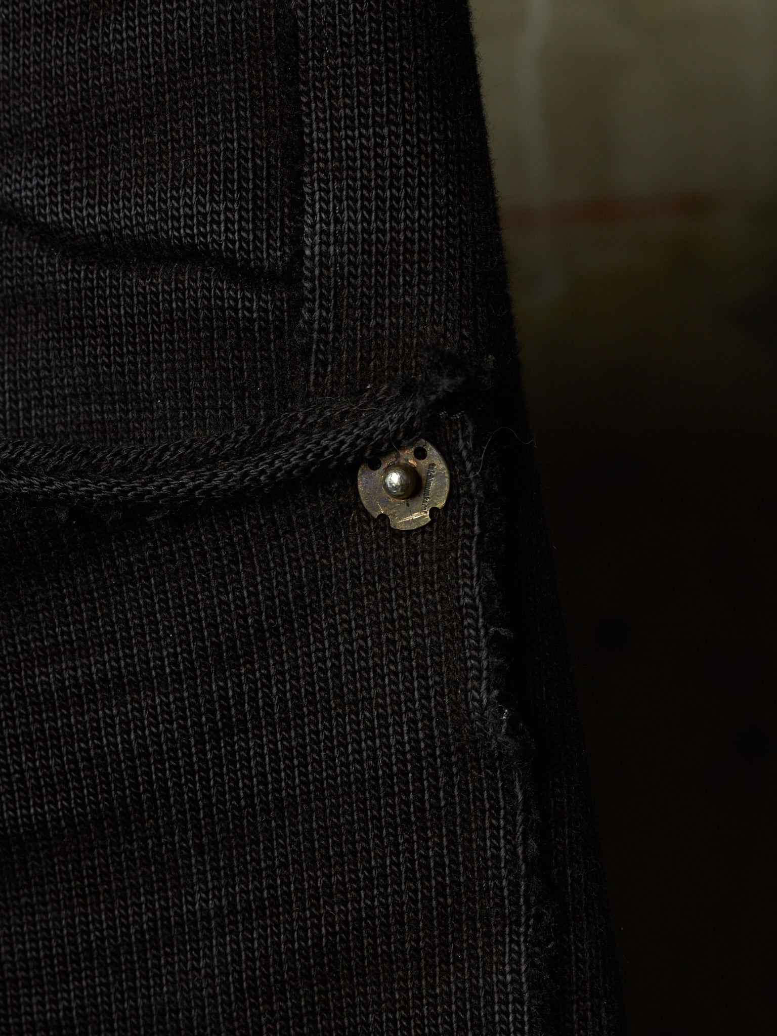 Close-up of a black ribbed knit garment, likely a sweater or jacket, showing a small metallic snap button detail.