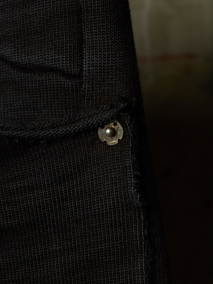 Close-up of a black ribbed knit garment, likely a sweater or jacket, showing a small metallic snap button detail.