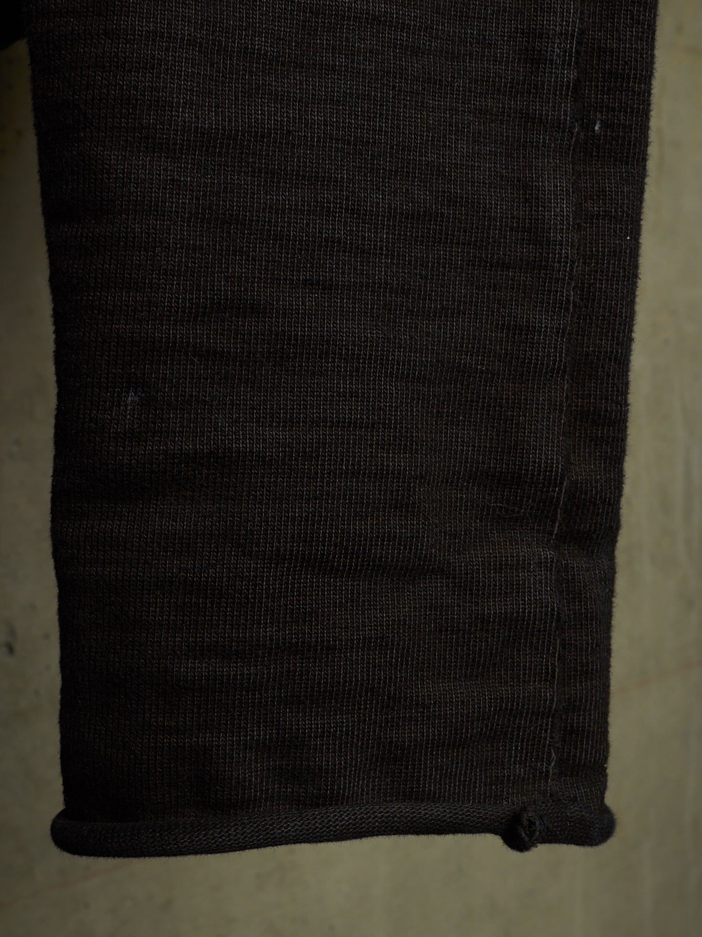 Close-up of a dark charcoal gray ribbed knit fabric cuff, showing the texture and rolled hem detail.