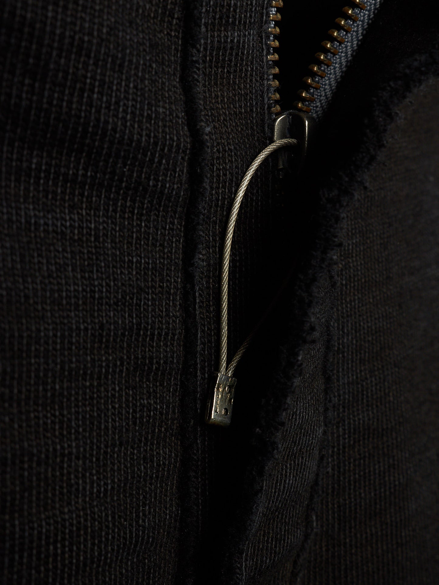 Close-up of a black ribbed knit garment featuring a silver metal zipper and a matching silver zipper pull cord.