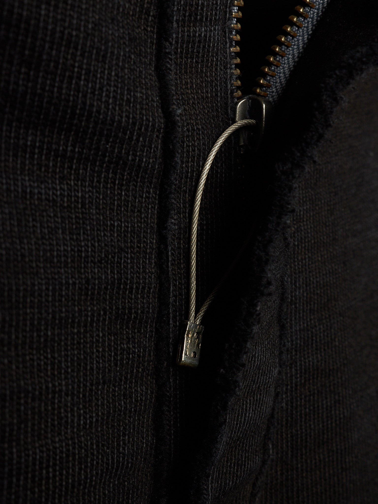 Close-up of a black ribbed knit garment featuring a silver metal zipper and a matching silver zipper pull cord.