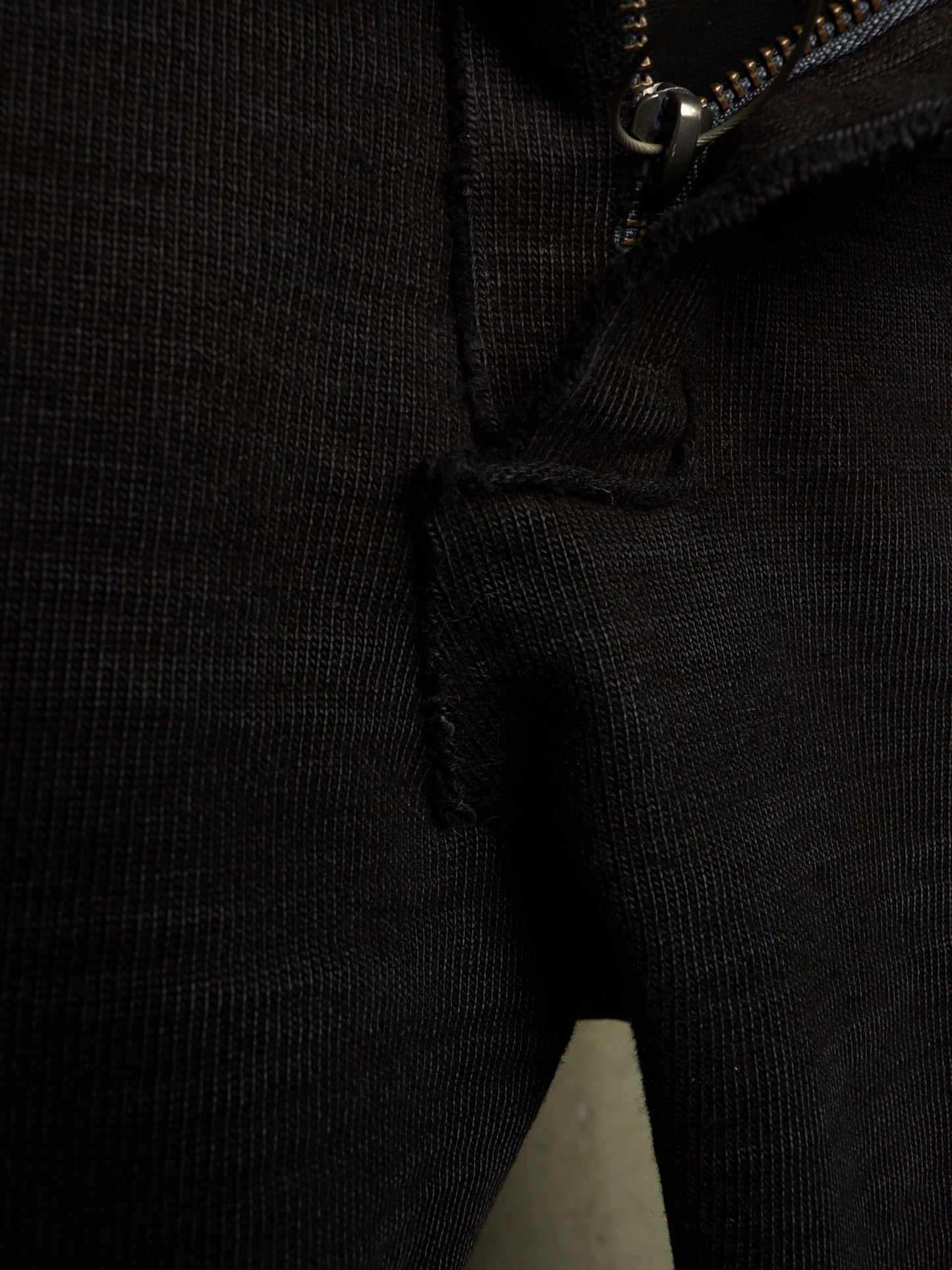 Close-up detail of a black ribbed knit garment, showing a zipper, seam, and textured fabric.