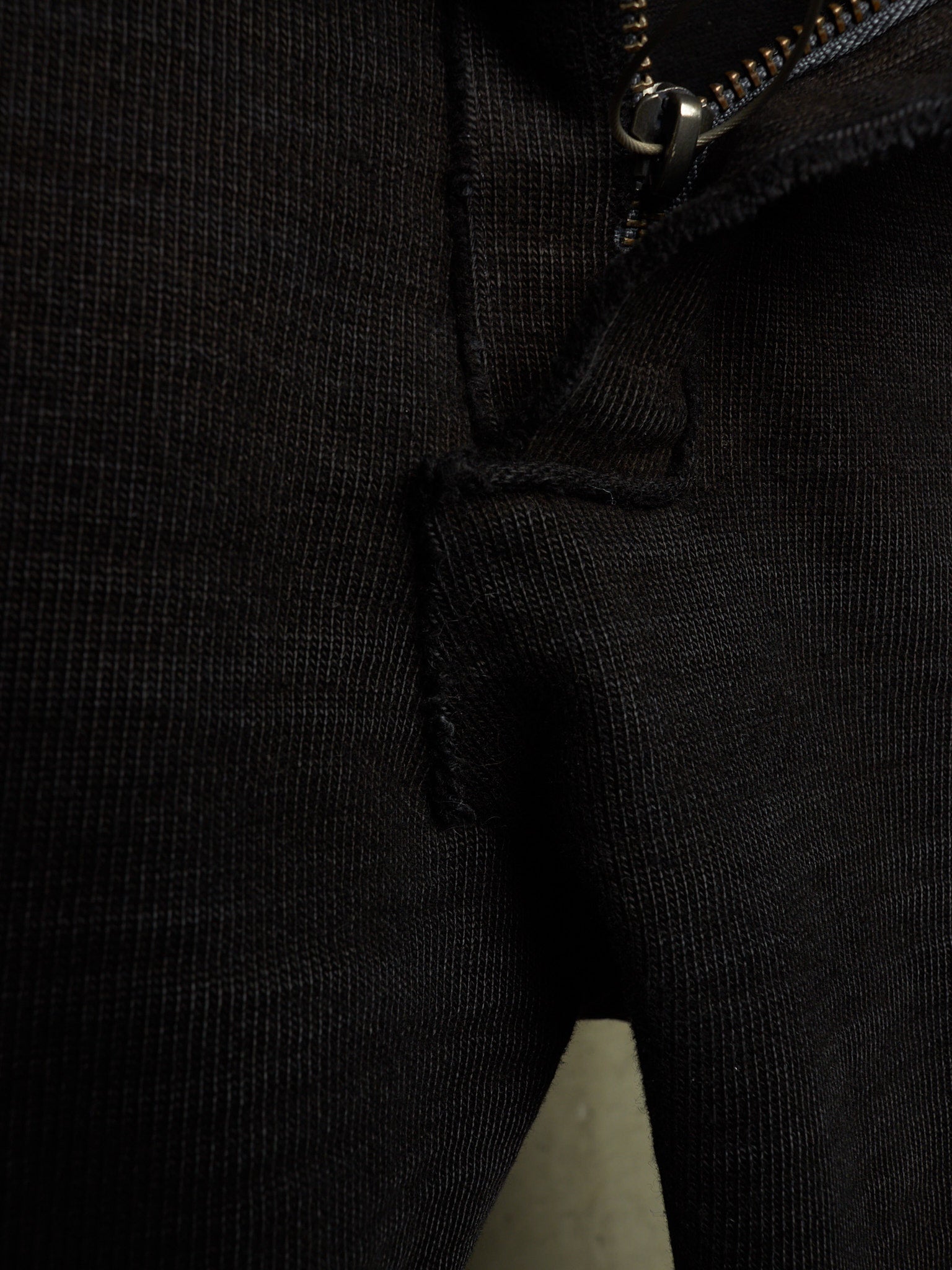 Close-up detail of a black ribbed knit garment, showing a zipper, seam, and textured fabric.