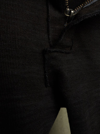 Close-up detail of a black ribbed knit garment, showing a zipper, seam, and textured fabric.