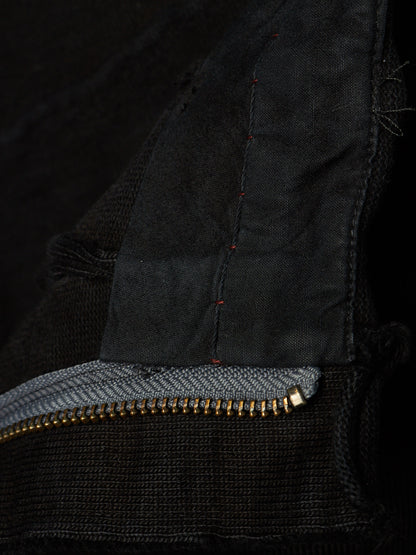 Close-up detail of a black knit garment showing a gold-tone zipper, a gray inner lining, and dark red contrast stitching.