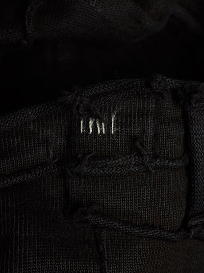 Close-up of a black woven textile with a small white embroidered logo reading 'MNT' on a dark background.