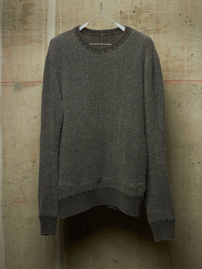 A dark gray textured knit sweater hanging on a white plastic hanger against a rustic concrete wall.