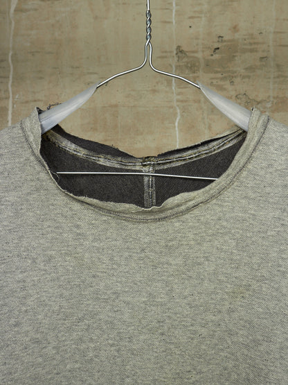 A close-up of a heather gray crewneck sweatshirt hanging on a white plastic hanger against a textured beige wall.