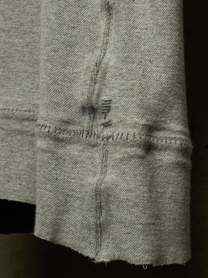 Close-up of a light gray knit fabric sleeve or cuff with visible stitching and a small dark embroidered detail near the center.