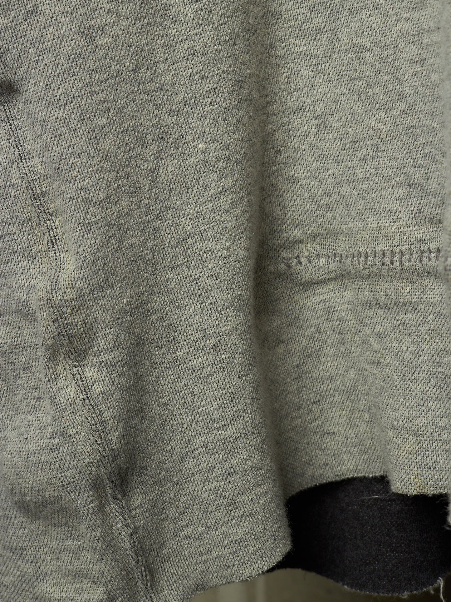 Close-up of a heather gray knit fabric garment, showing the texture and hem detail.