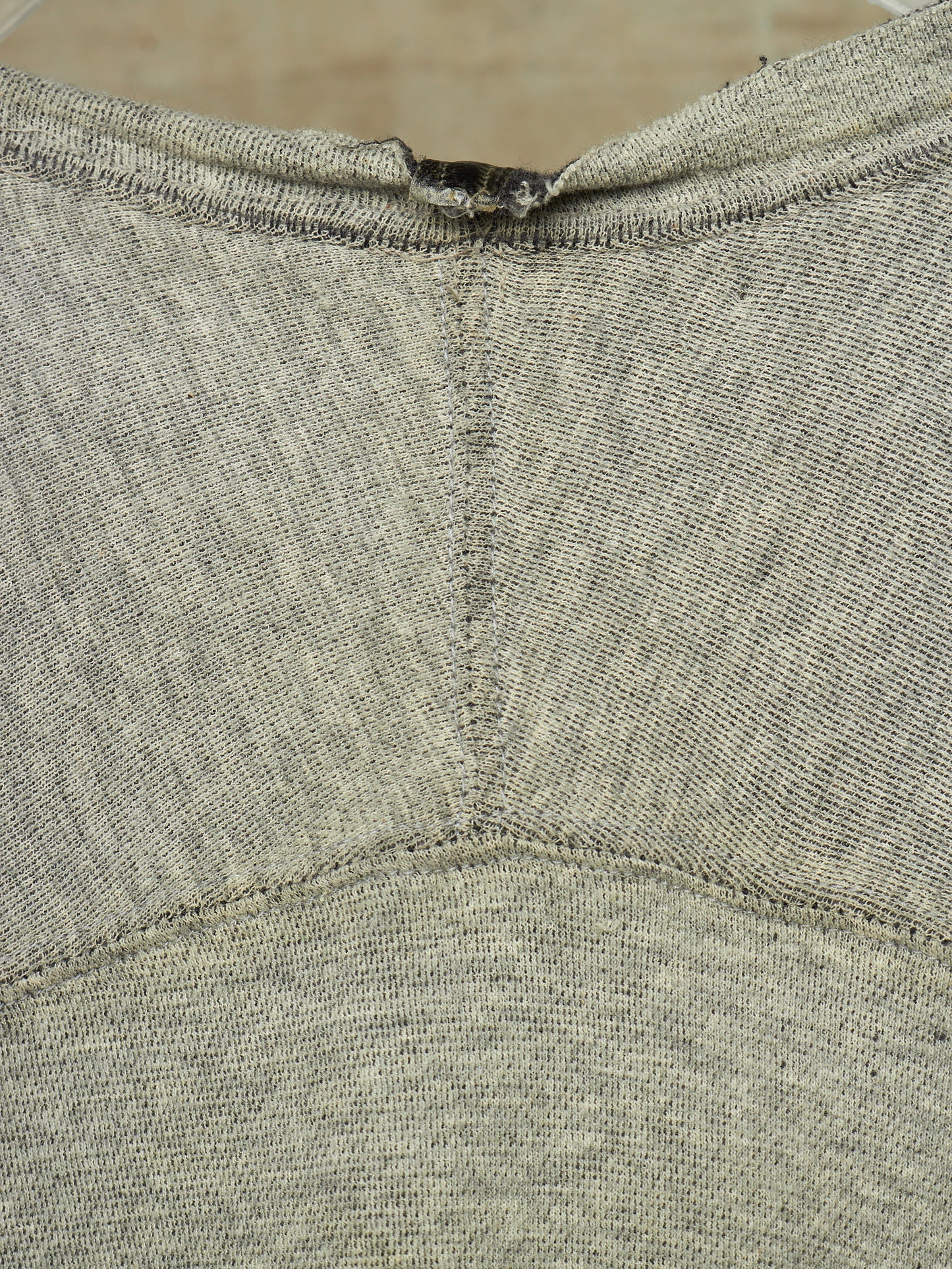 Close-up of a heather gray knit garment, showing the back neckline with a small dark tag or label attached at the collar.