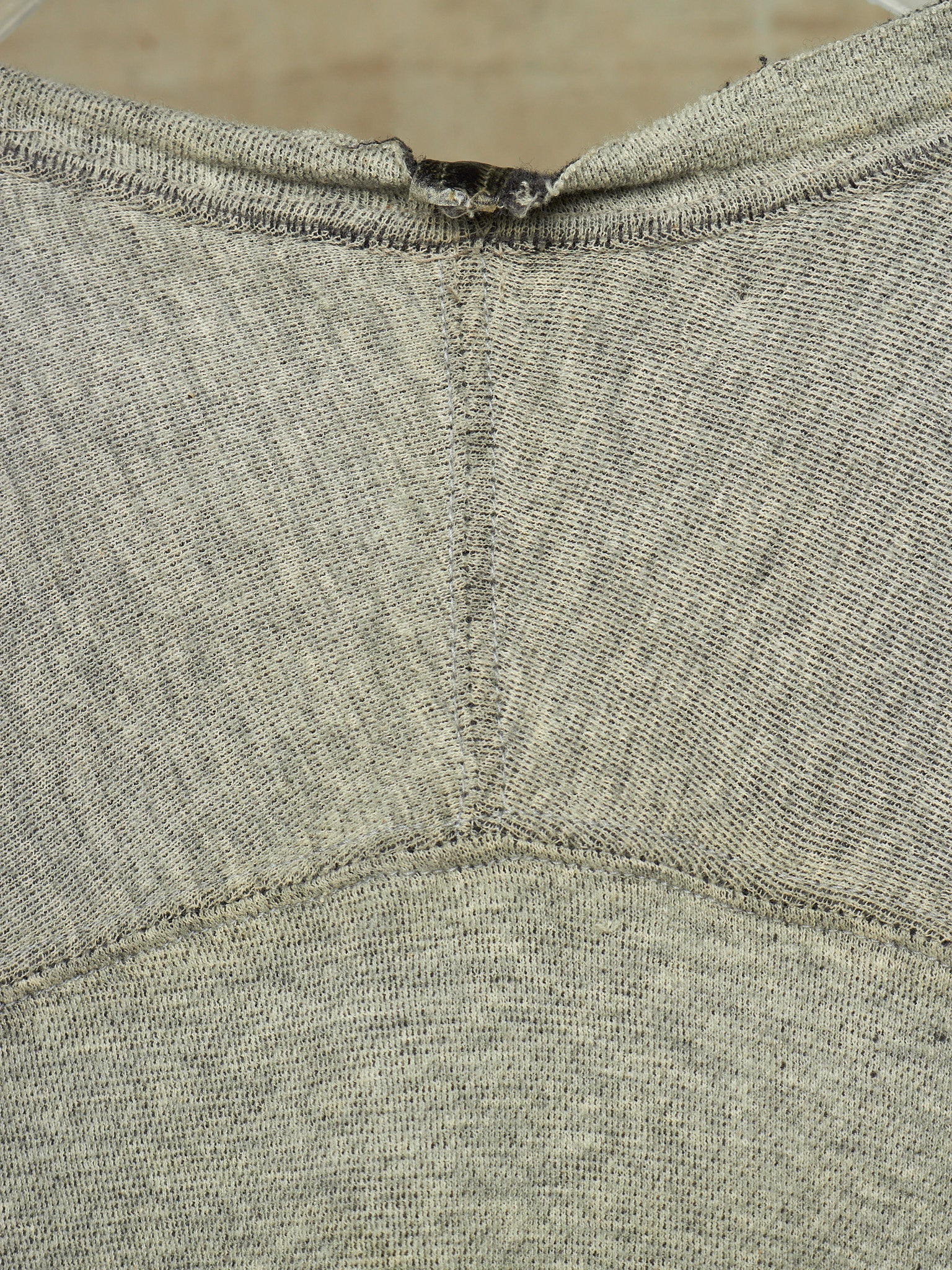 Close-up of a heather gray knit garment, showing the back neckline with a small dark tag or label attached at the collar.