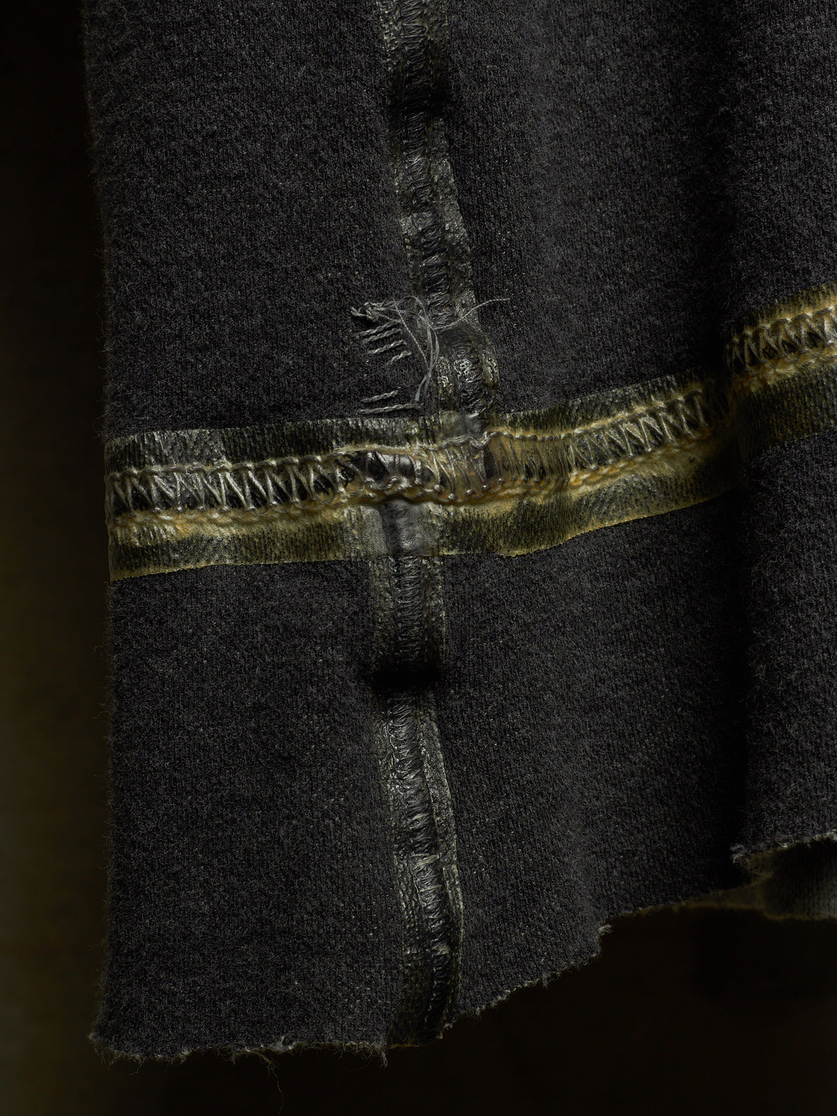 Close-up of a dark charcoal gray wool fabric with a decorative horizontal band featuring metallic gold and bronze braided stitching.