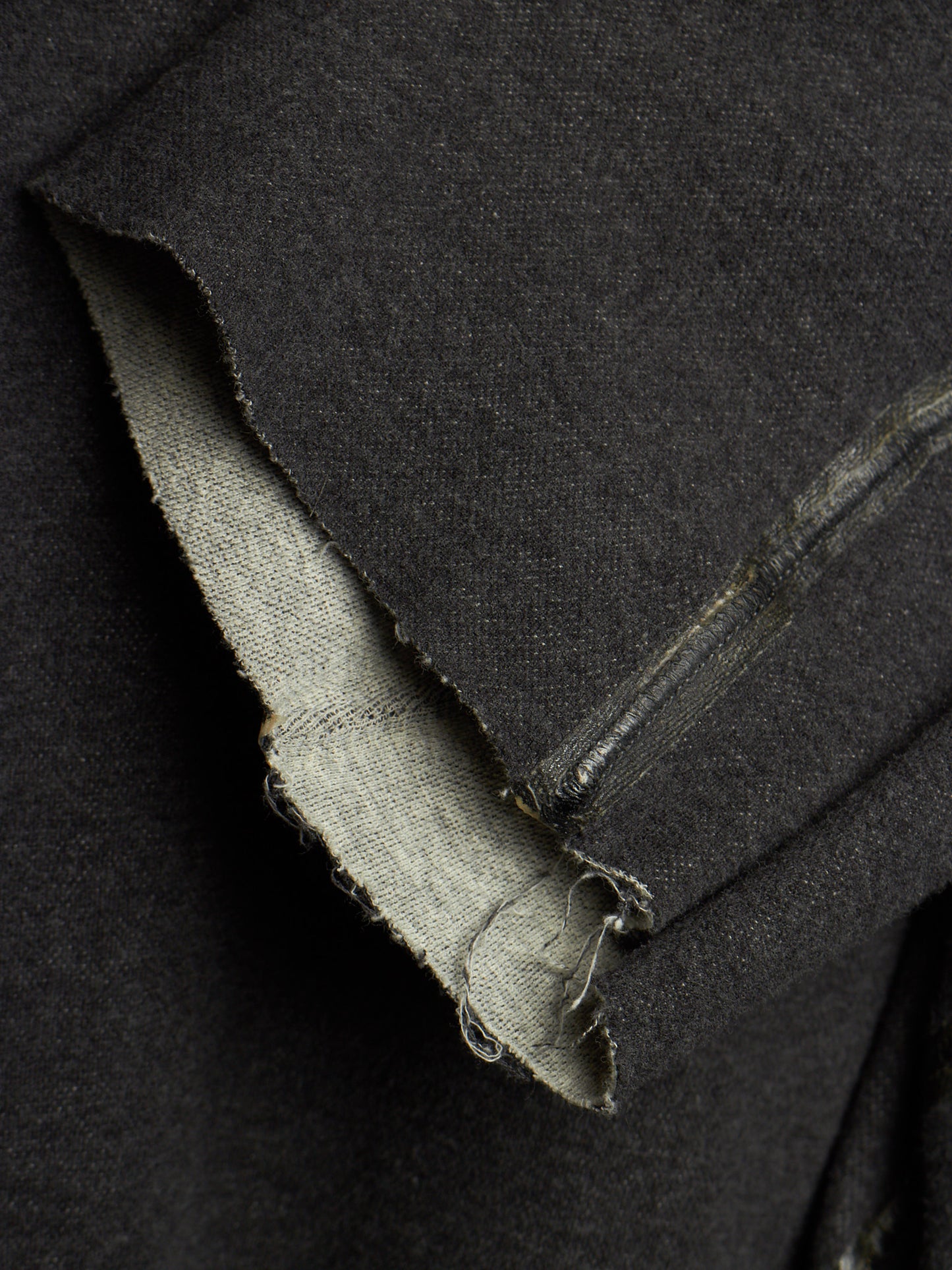 Close-up of a dark charcoal gray fabric garment, showing a raw, frayed hem and the lighter inner lining.